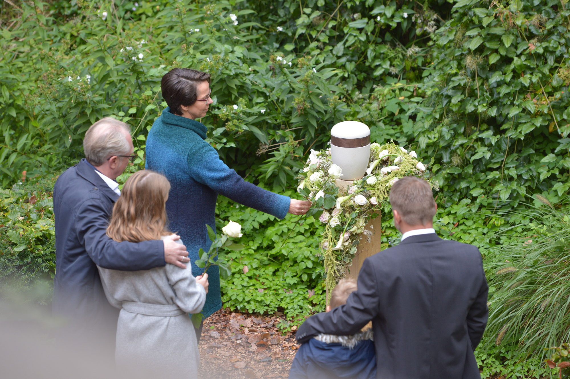 Mehere Personen stehen vor einer Urn bei einer Trauerfeier.